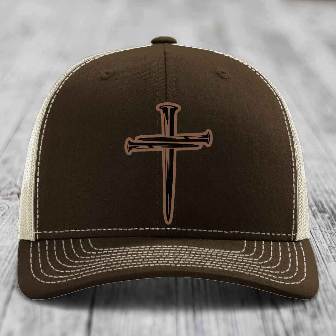 Tan trucker hat with black cross and nail patch on front, black mesh back.