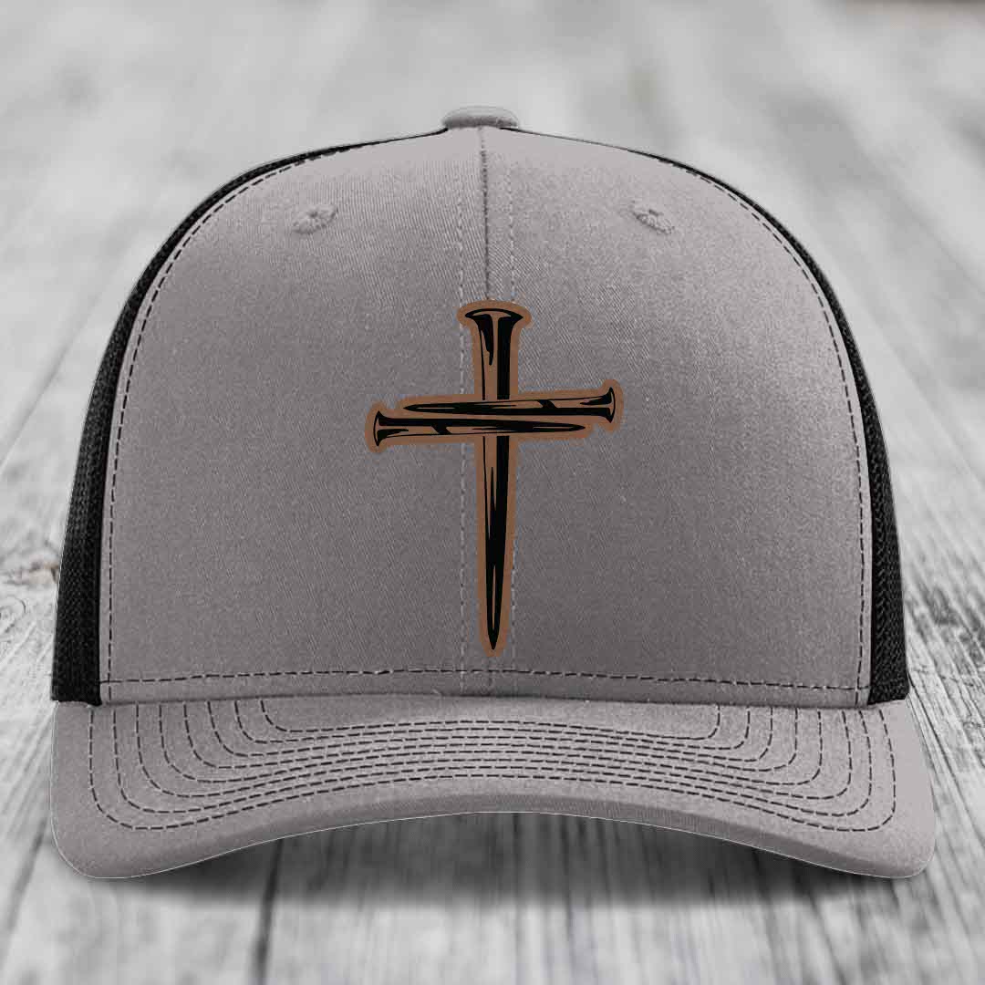 Grey trucker hat with blue mesh sides and a cross made of nails patch on front.