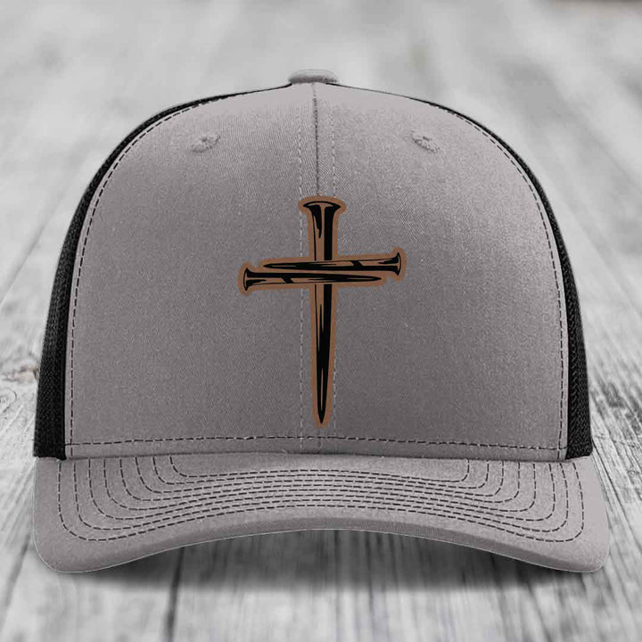 Grey trucker hat with blue mesh sides and a cross made of nails patch on front.