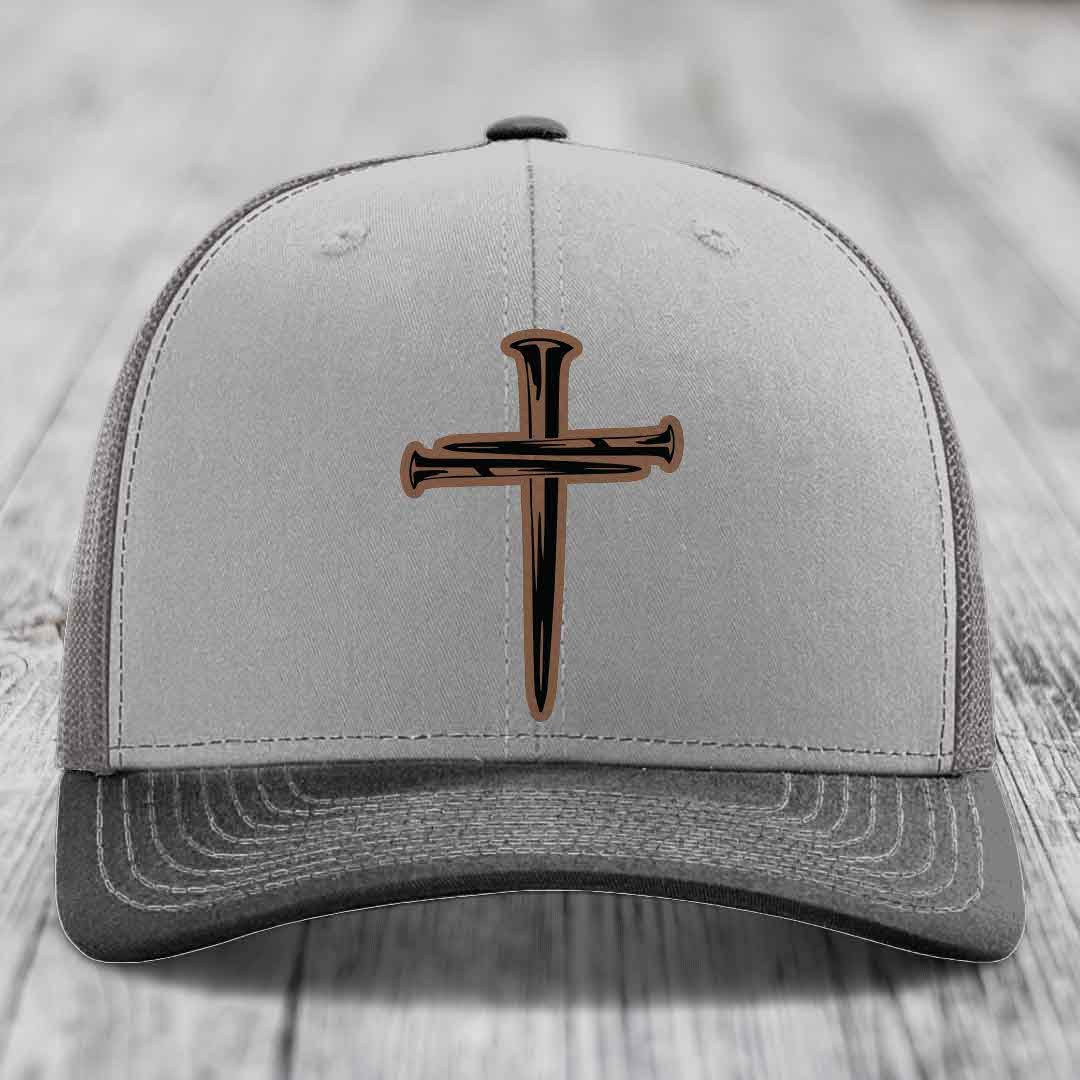Grey and beige trucker hat with a cross made of nails patch on front.