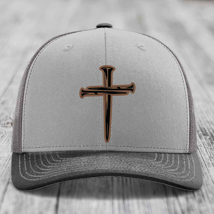 Grey and beige trucker hat with a cross made of nails patch on front.