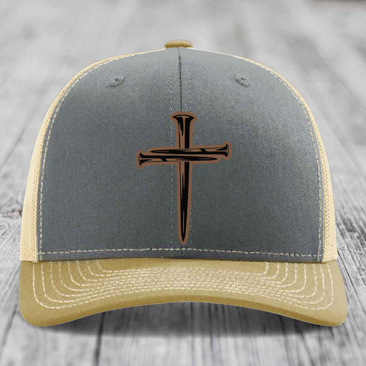 Grey trucker hat with a cross made of nails patch on front.