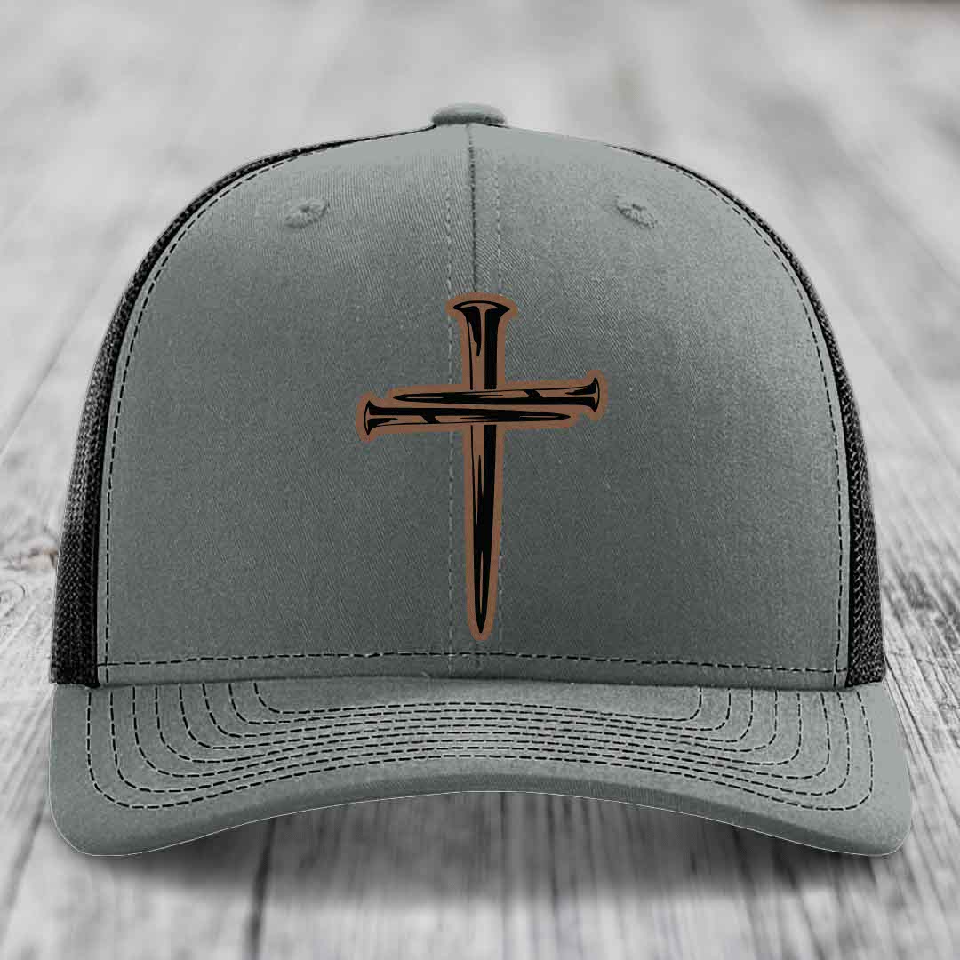 Grey trucker hat with black and brown cross of nails leather patch on front.