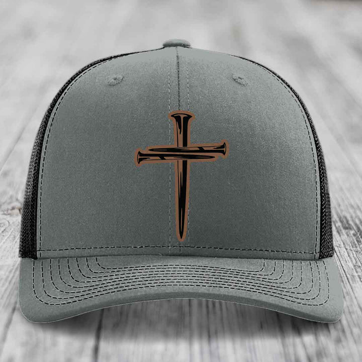 Grey trucker hat with black and brown cross of nails leather patch on front.