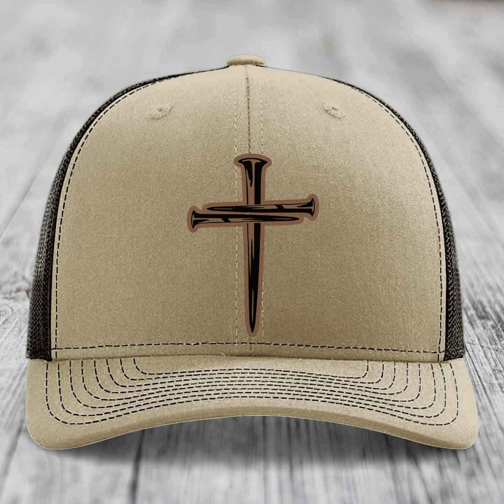 Tan trucker hat with black and brown cross of nails patch on front.