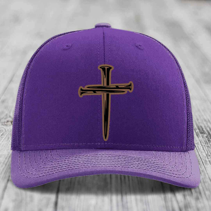 Red trucker hat with black mesh back and a cross of nails patch on front.