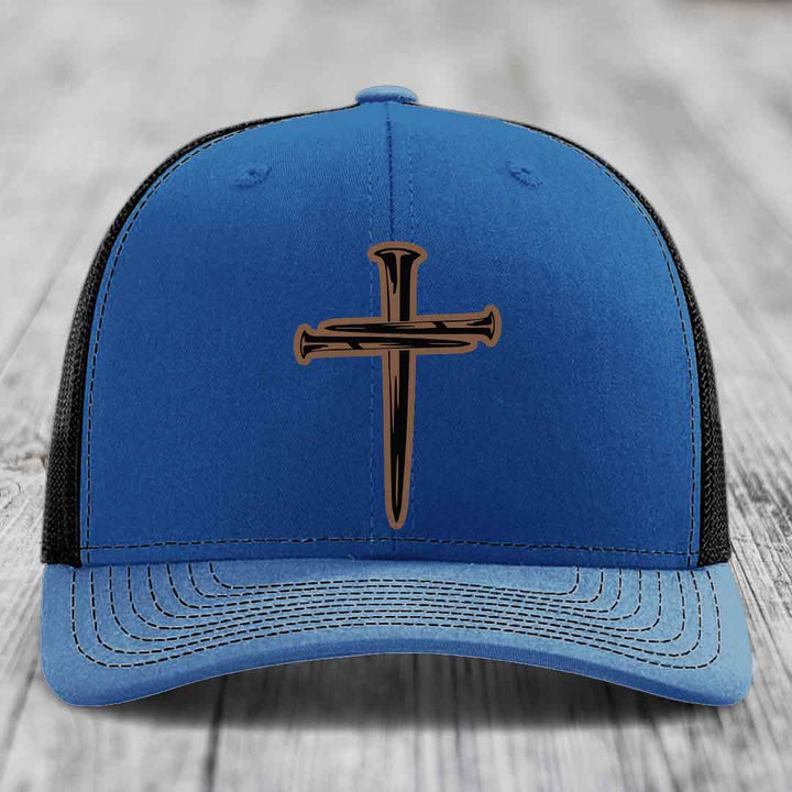 Blue and red trucker hat with a cross made of nails patch on front.
