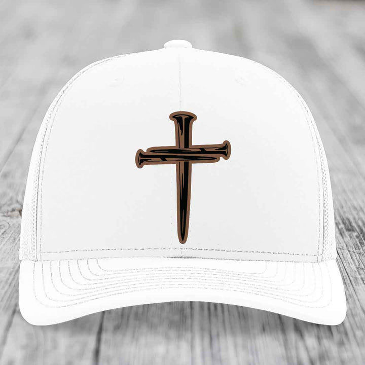 Camouflage trucker hat with a cross made of nails patch in tan and black.