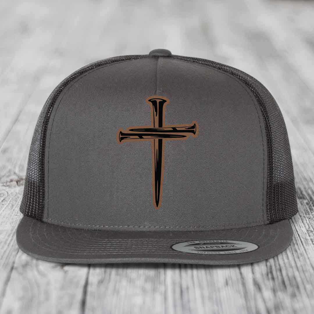 Grey trucker hat with black and brown cross of nails leather patch on front.