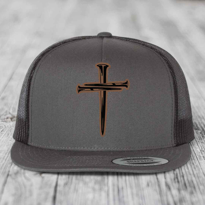 Grey trucker hat with black and brown cross of nails leather patch on front.