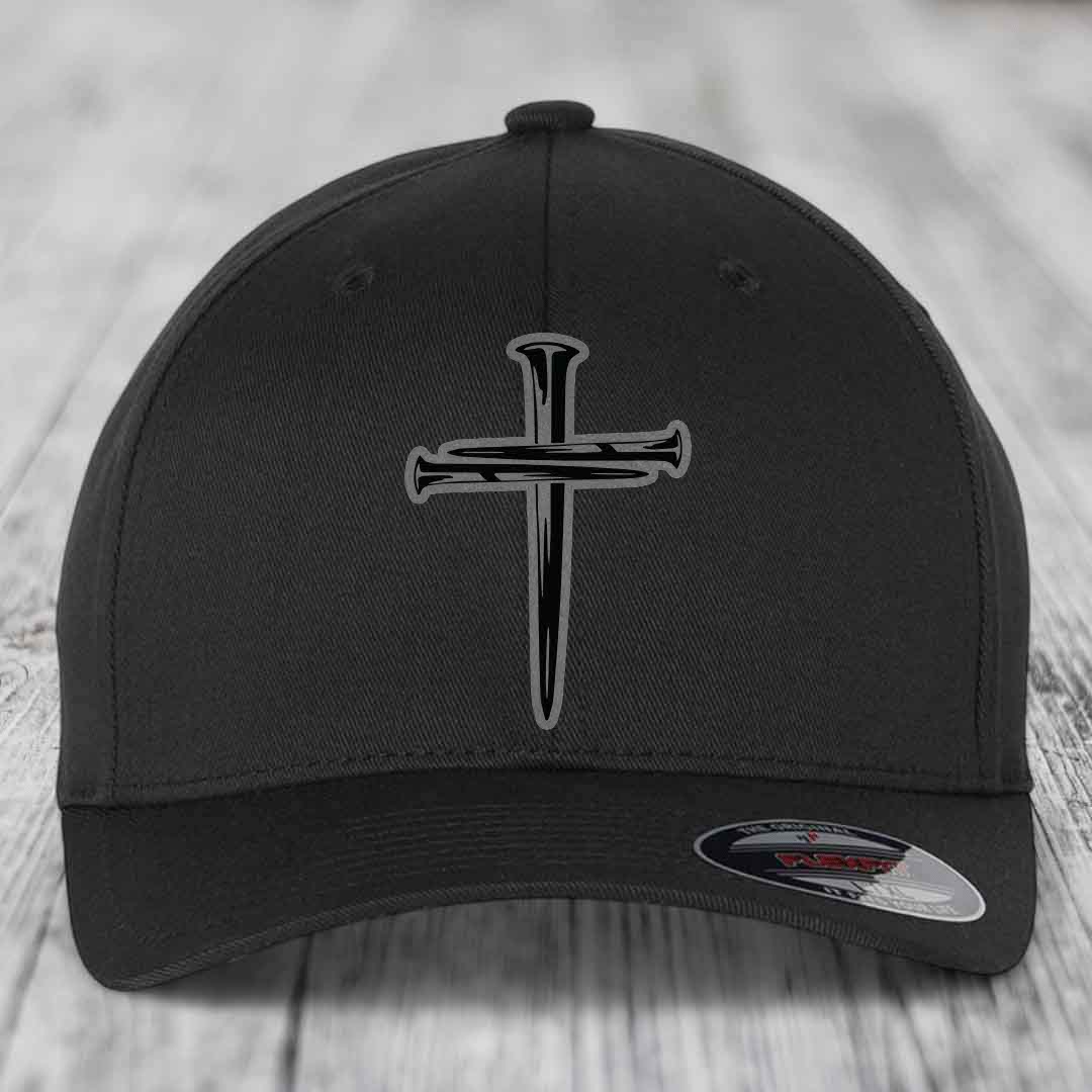 Black baseball cap with a cross of nails patch on front, displayed on wooden surface.
