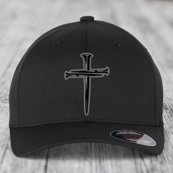 Black baseball cap with a cross of nails patch on front, displayed on wooden surface.