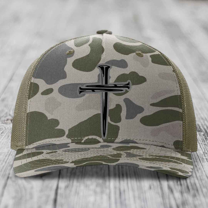 Camouflage trucker hat with black cross of nails patch on front.