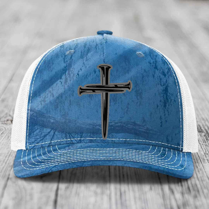 Camouflage trucker hat with black cross of nails patch on front.