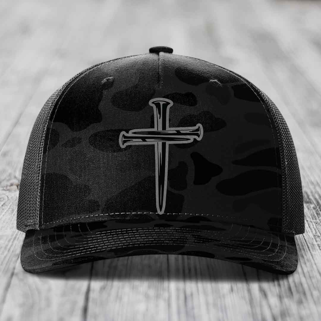 Camouflage trucker hat with black cross of nails patch on front.