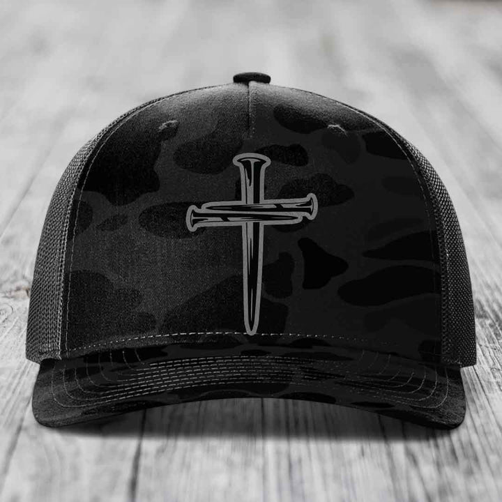 Camouflage trucker hat with black cross of nails patch on front.
