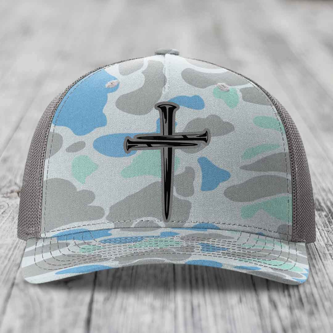 Camouflage trucker hat with a cross made of nails patch on front.