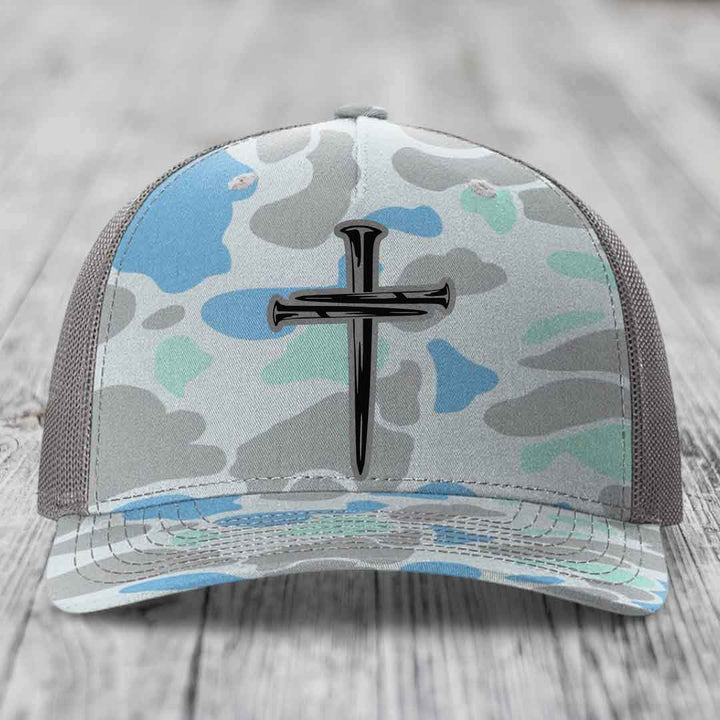 Camouflage trucker hat with a cross made of nails patch on front.