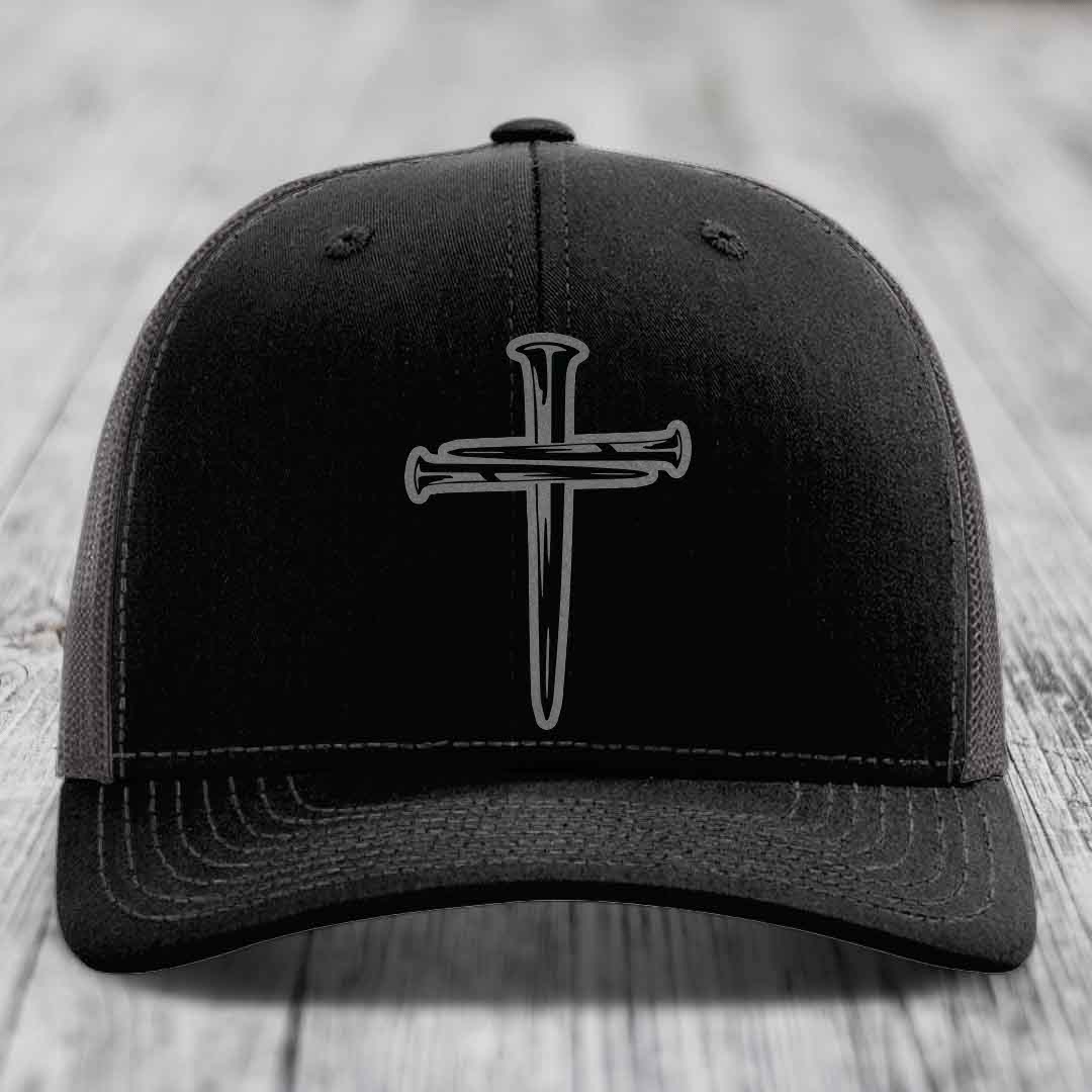 Black trucker hat with white stitching and a cross of nails patch on front.