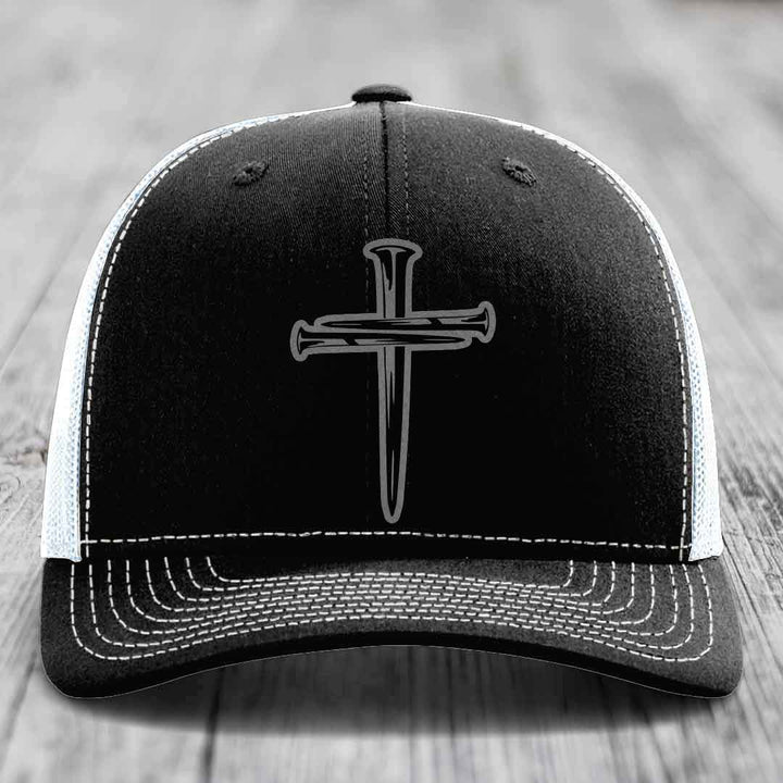 Black and grey trucker hat with a cross made of nails patch on front.