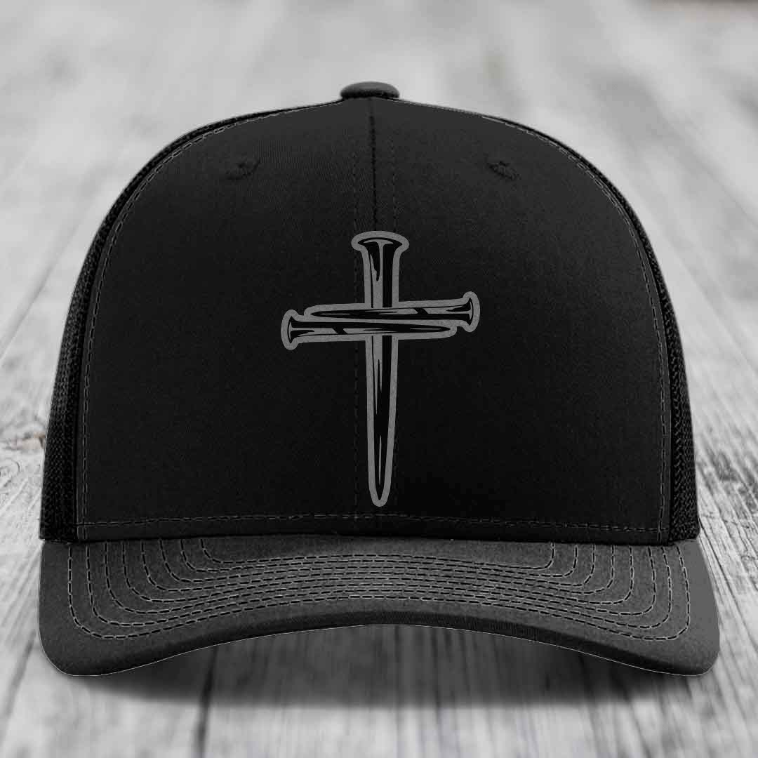 Tan baseball cap with blue mesh sides and a black cross made of nails patch on front.