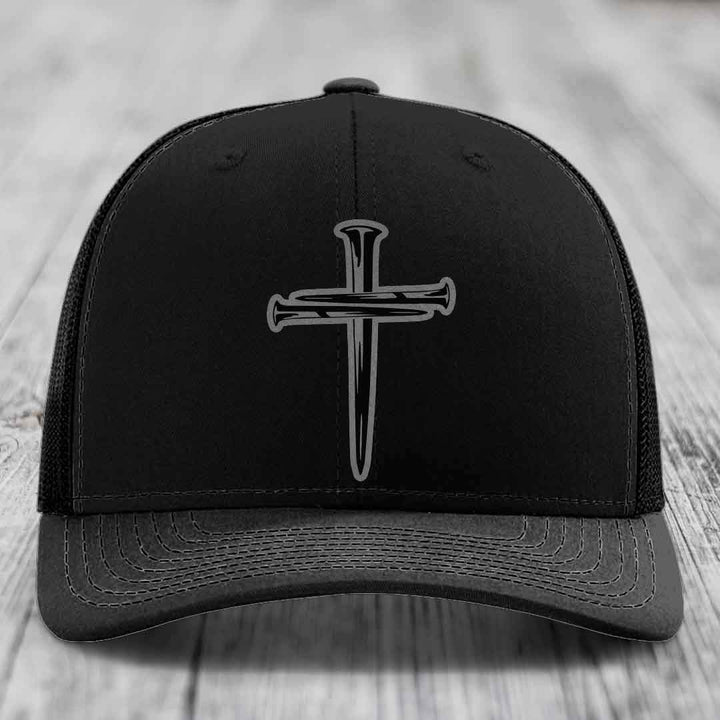 Tan baseball cap with blue mesh sides and a black cross made of nails patch on front.