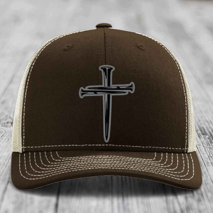 Tan trucker hat with black mesh back and a black cross of nails patch on front.