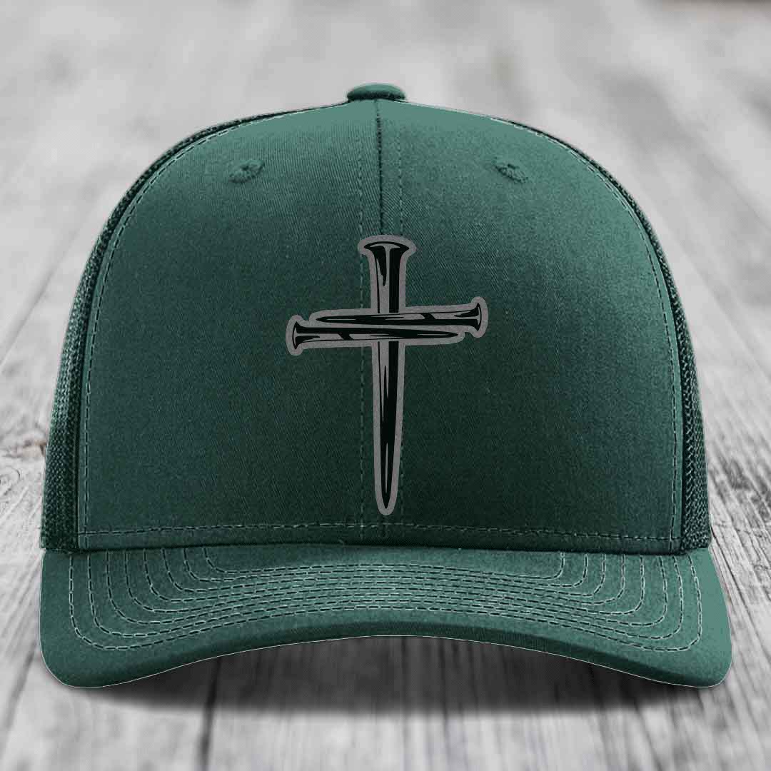 Grey trucker hat with black cross of nails patch on front, placed on wooden surface.