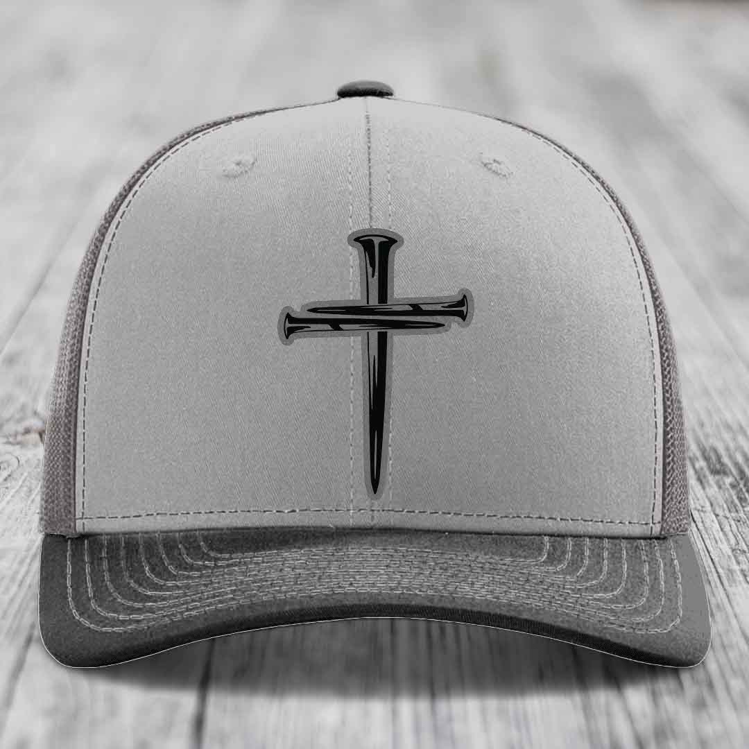 Grey and beige trucker hat with black cross of nails patch on front.