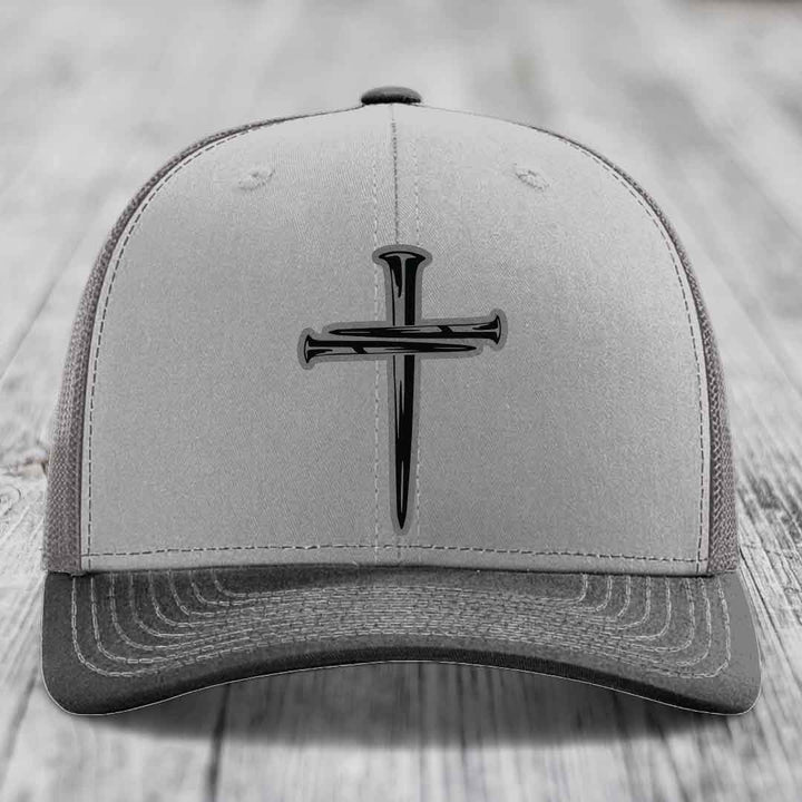 Grey and beige trucker hat with black cross of nails patch on front.