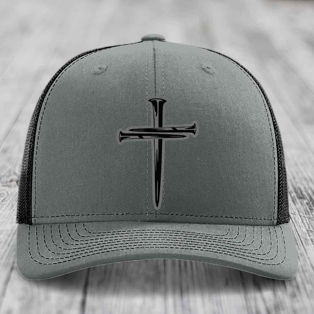 Grey trucker hat with black cross of nails patch on front, white mesh back and stitching.