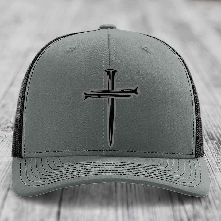 Grey trucker hat with black cross of nails patch on front, white mesh back and stitching.