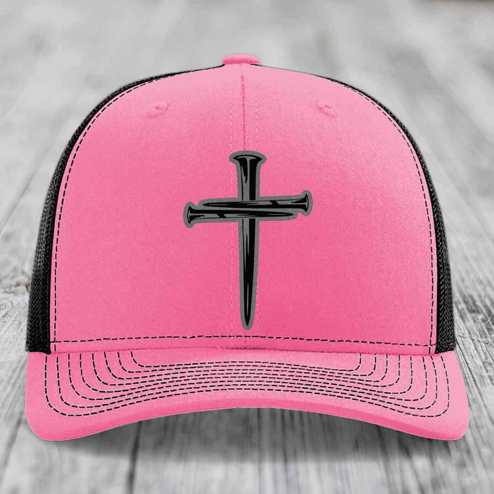 Green trucker hat with black cross of nails patch and white stitching.