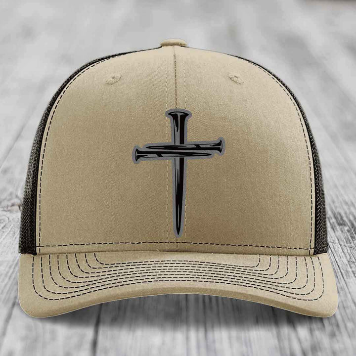 Tan trucker hat with black cross of nails patch on front, white mesh back and stitching.