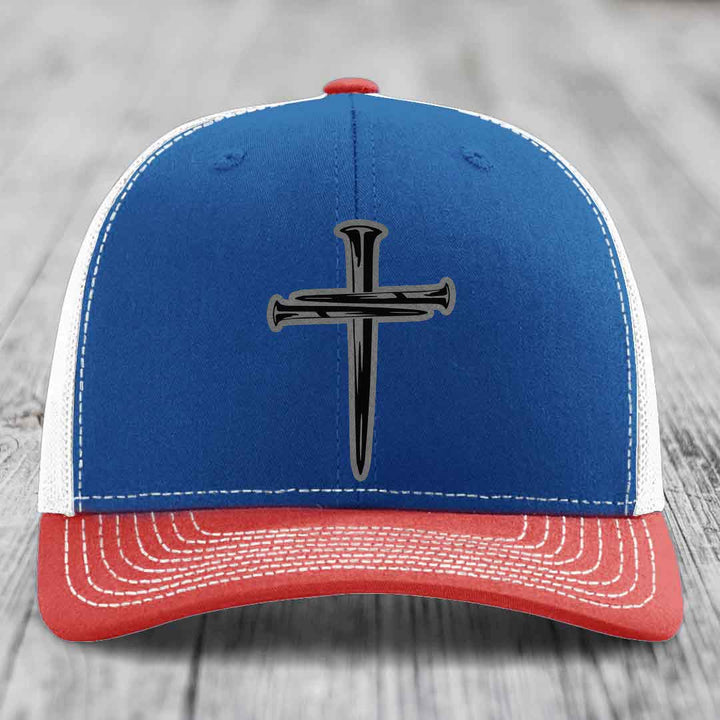 White trucker hat with black cross made of nails patch on front.