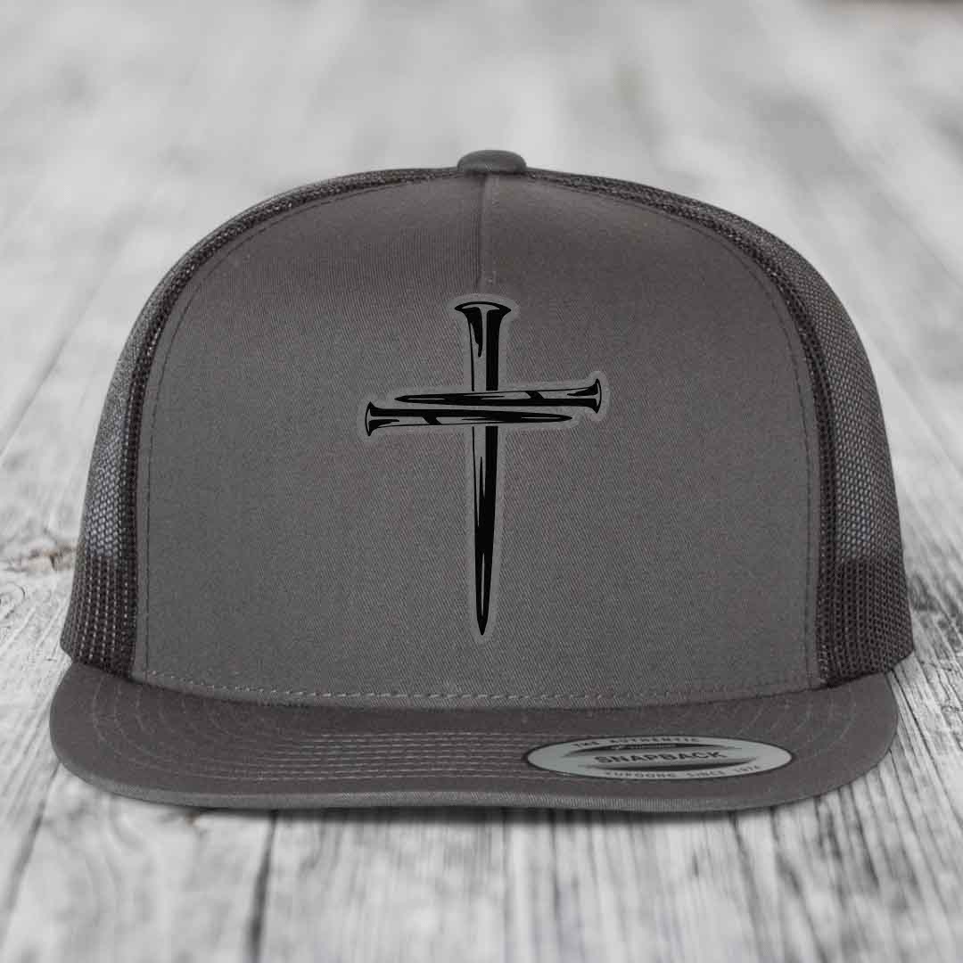 Grey trucker hat with black cross of nails patch on front, black mesh back, and snapback closure.