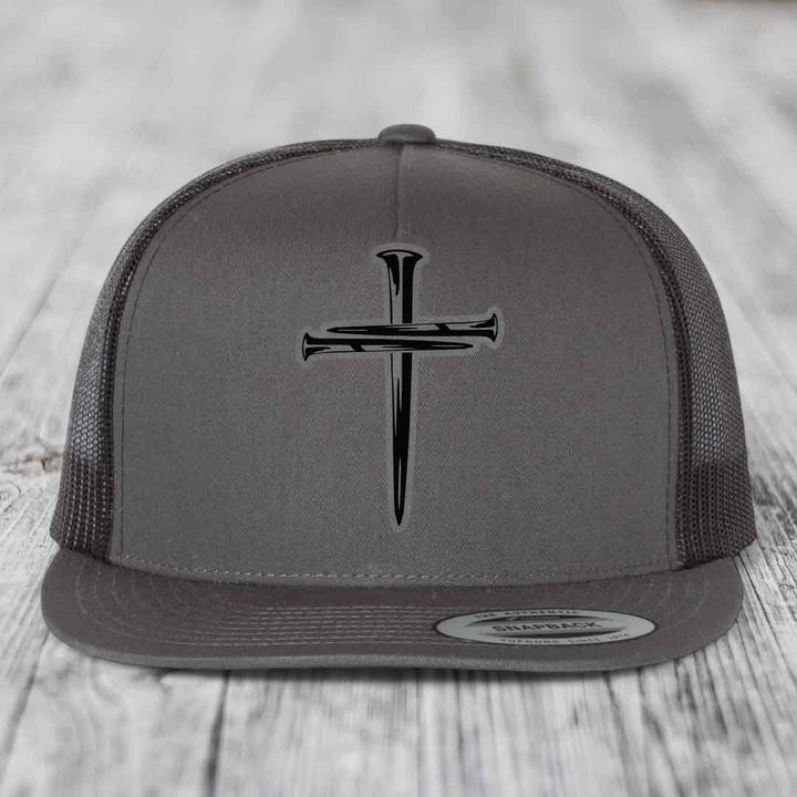 Grey trucker hat with black cross of nails patch on front, black mesh back, and snapback closure.