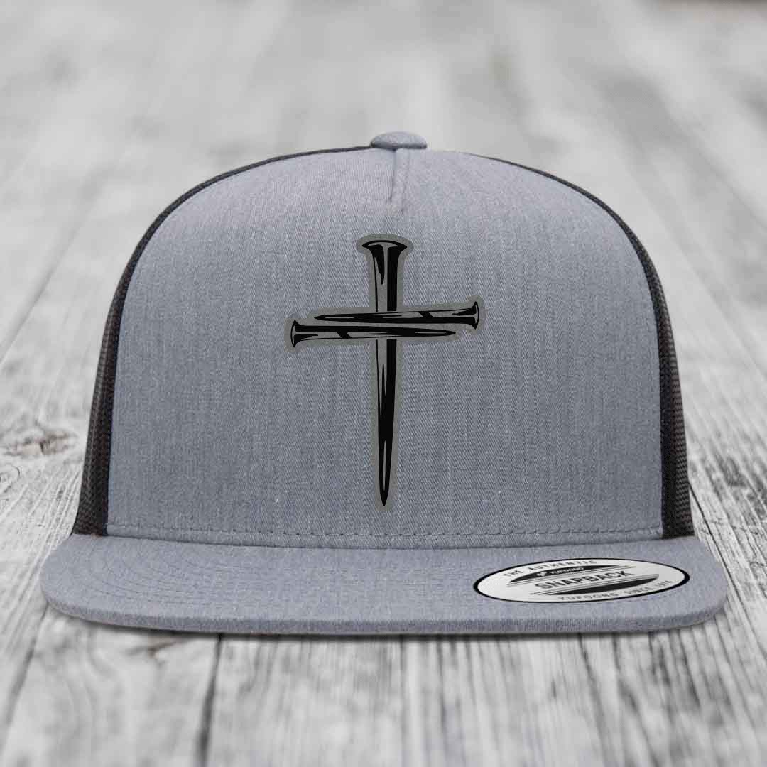 Grey trucker hat with black cross of nails patch on front, white mesh back, and snapback closure.