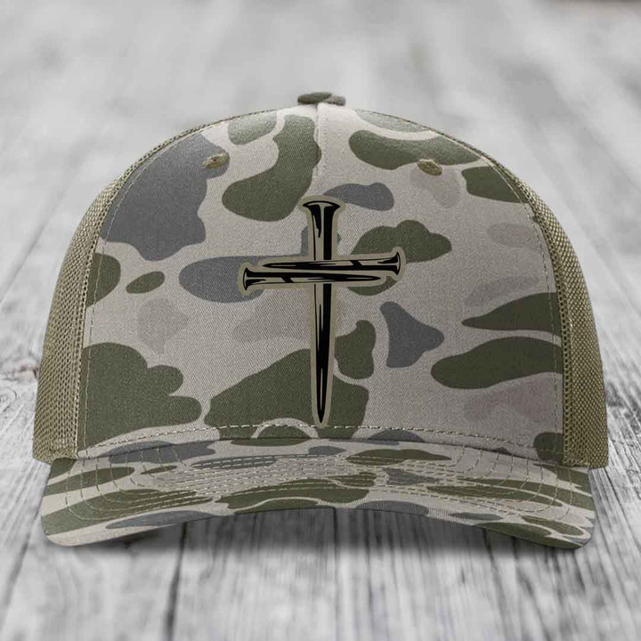 Camouflage trucker hat with black cross of nails patch on front.