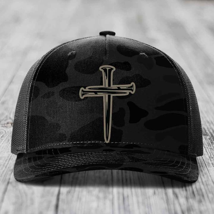 Camouflage trucker hat with black cross of nails patch on front.
