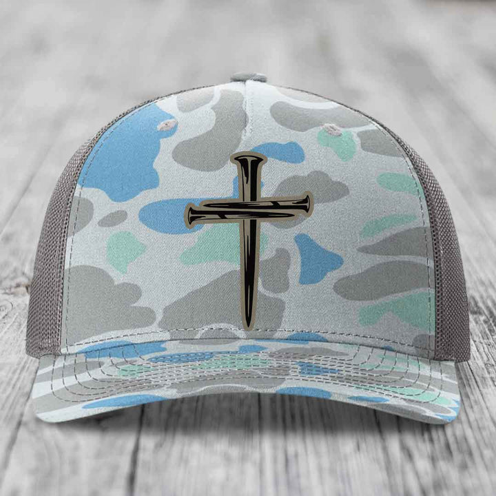 Camouflage trucker hat with a cross made of nails patch on front.