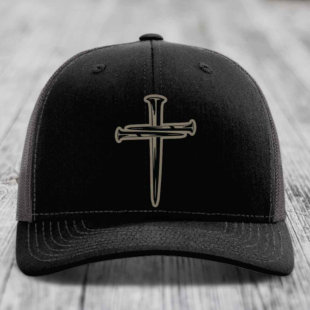 Black trucker hat with white stitching and a cross of nails patch on front.