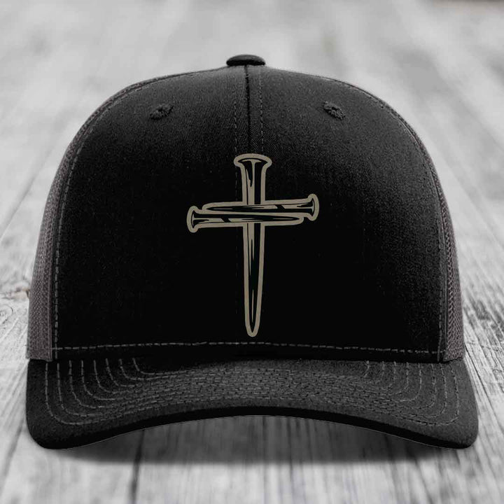 Black trucker hat with white stitching and a cross of nails patch on front.