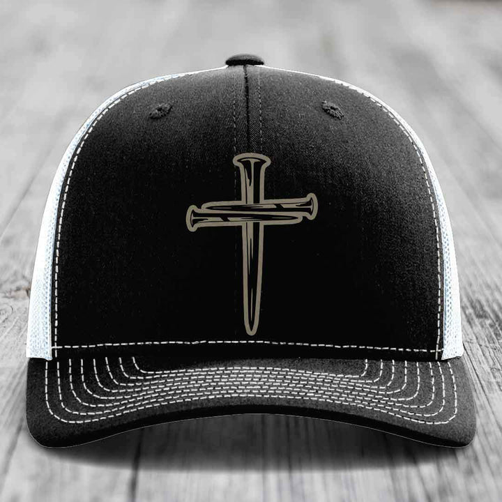Black trucker hat with silver cross of nails patch on front, white mesh back and gray brim.