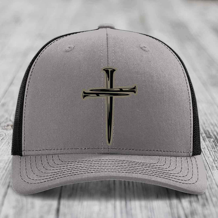 Grey trucker hat with blue mesh sides and a black cross of nails patch on front.