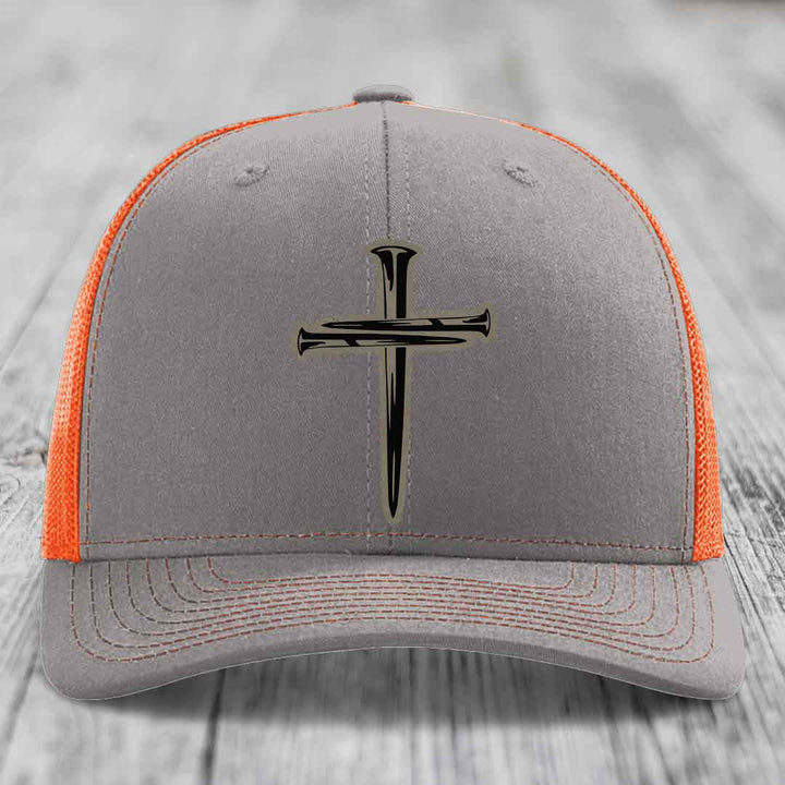 Grey trucker hat with black cross of nails patch and pink mesh sides.