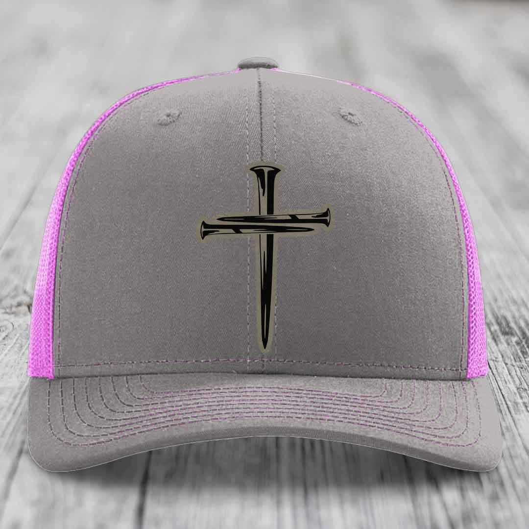 Grey trucker hat with black cross of nails patch and yellow stitching on mesh sides.