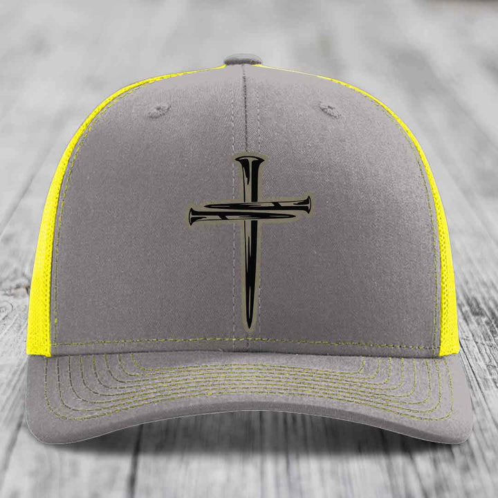 Brown trucker hat with black cross made of nails patch on front.