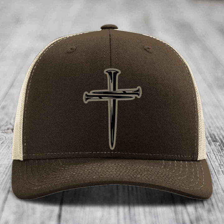 Dark green trucker hat with a cross made of nails patch on front.
