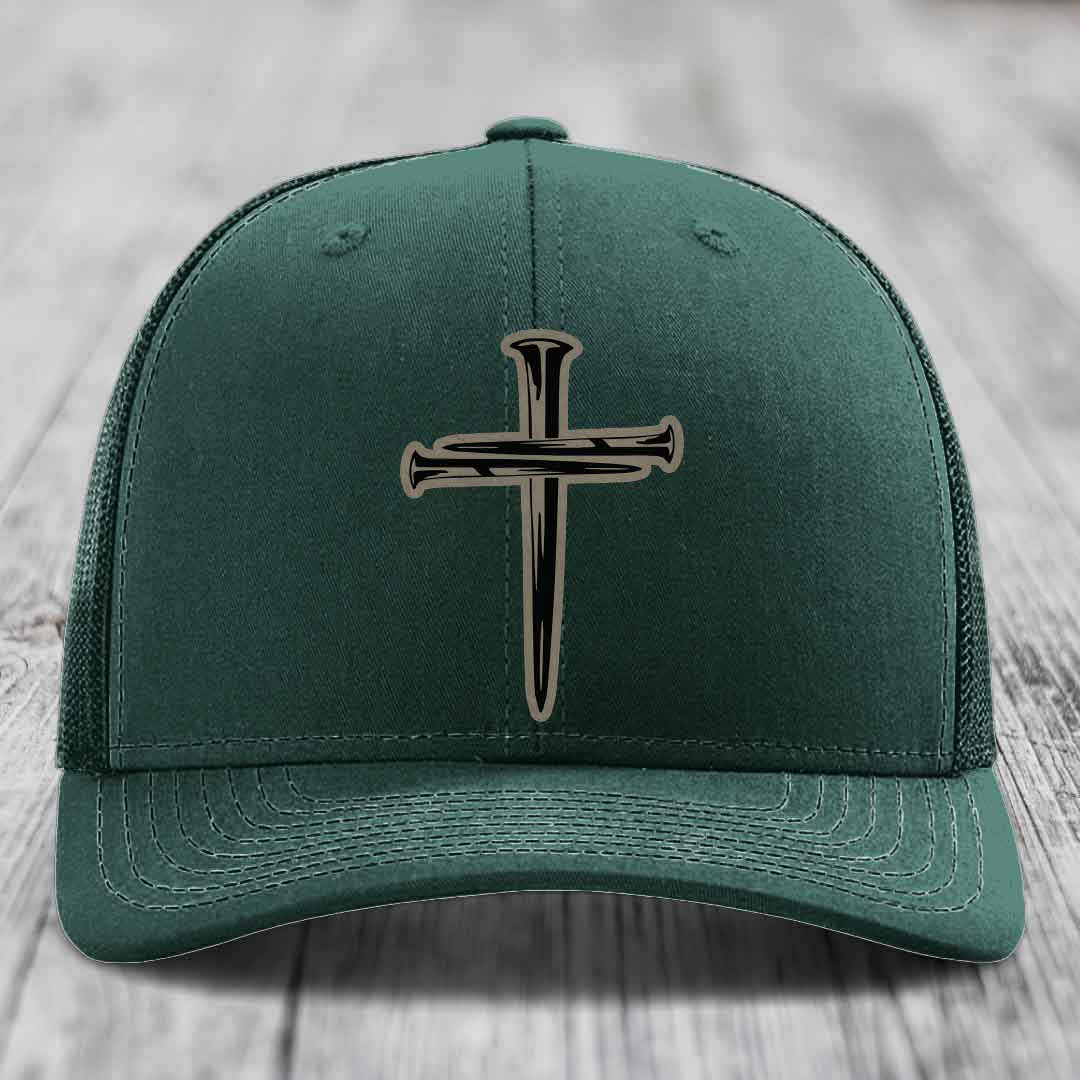 Grey trucker hat with black cross of nails patch on front, placed on wooden surface.